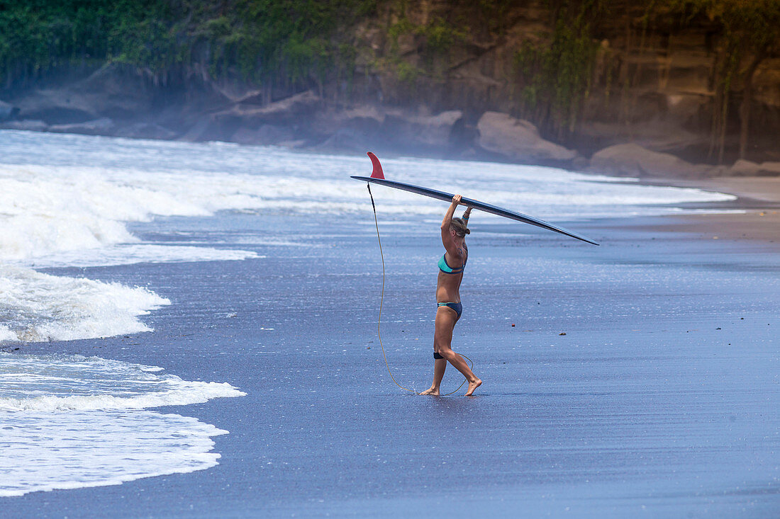 Young woman with surfboard on a beach.