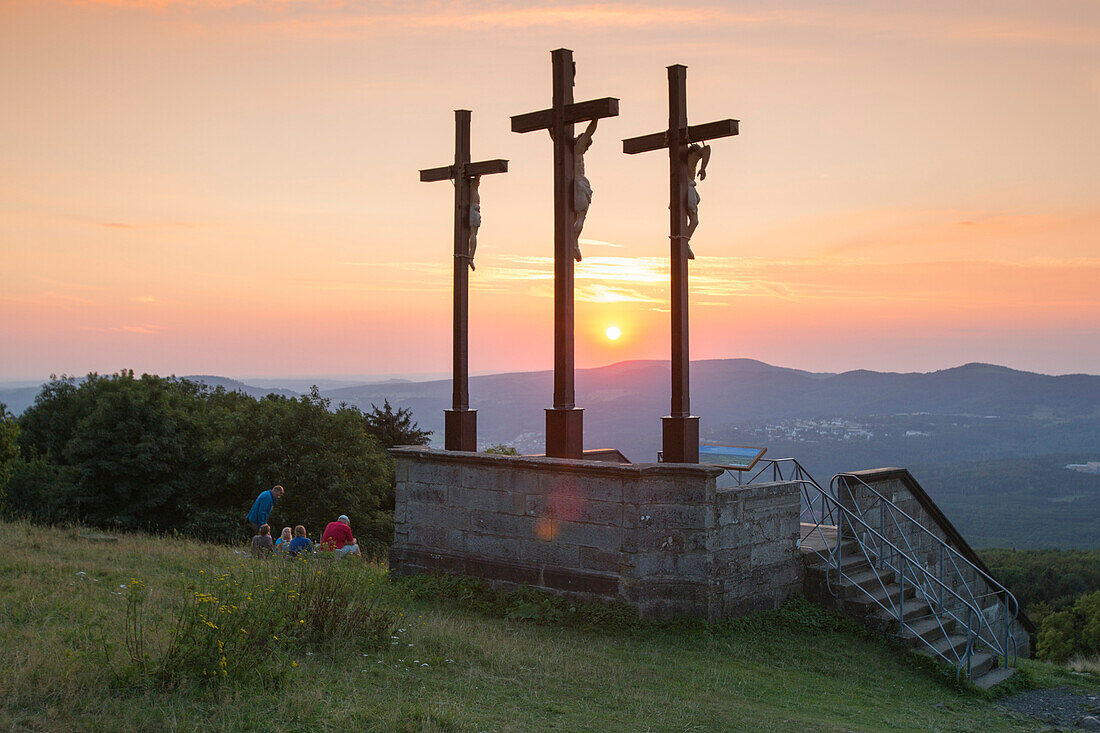Participants of pilgrimage from Würzburg enjoy a picnic near summit cross on Kreuzberg mountain at sunset