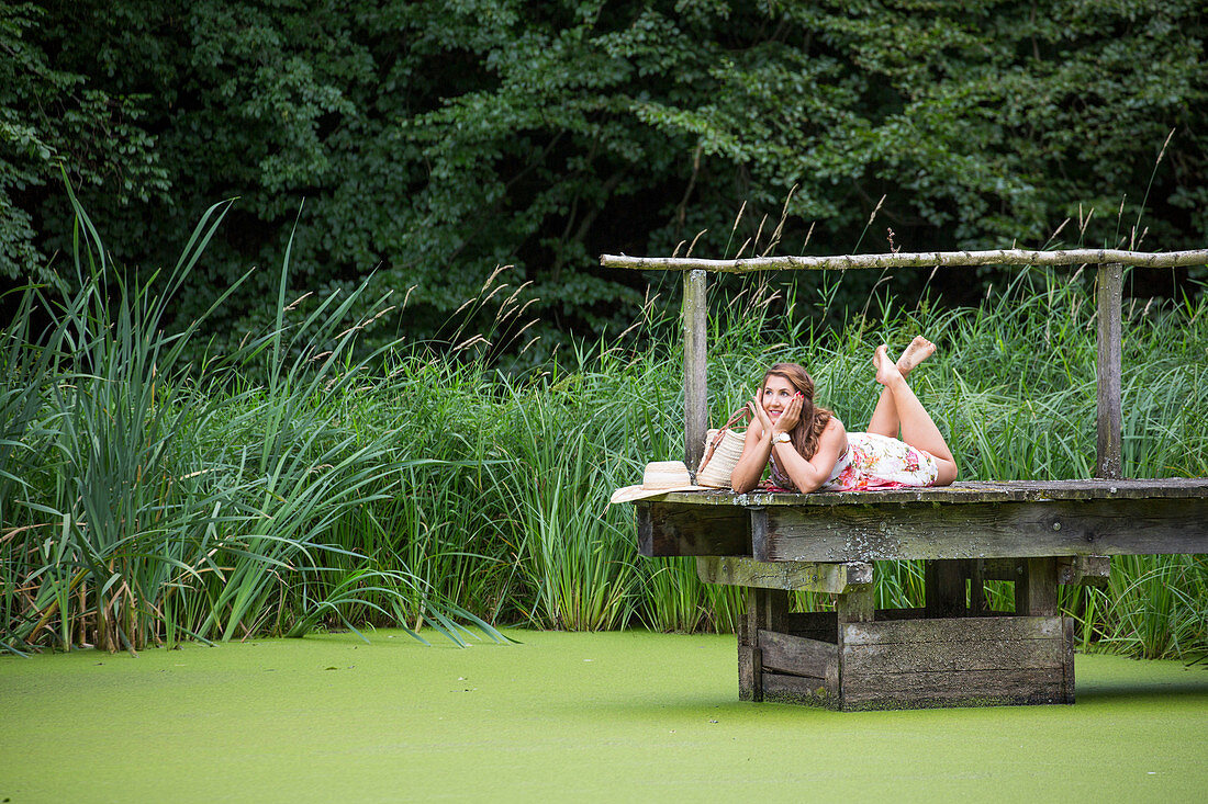 Junge Frau im Sommerkleid entspannt sich auf Steg am Teich, Haunetal, Rhön, Hessen, Deutschland [MR]