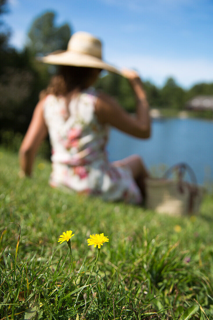 Junge Frau im Sommerkleid entspannt sich auf Wiese mit Löwenzahn am Guckaisee unterhalb der Wasserkuppe, Poppenhausen Rodholz, Rhön, Hessen, Deutschland