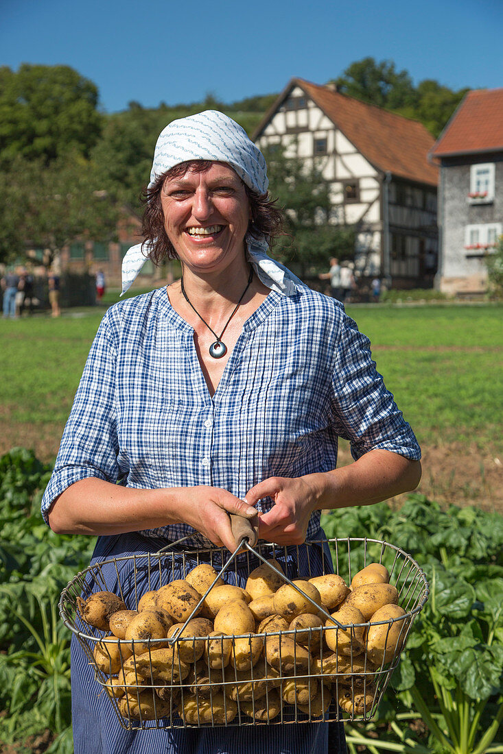 Woman in traditional attire with basket of potatoes during Museumsfest celebration at Fränkisches Freiluftmuseum Fladungen open air museum