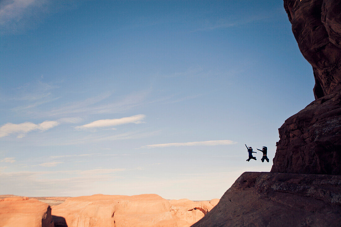 Two people jump for joy while hiking in the desert.