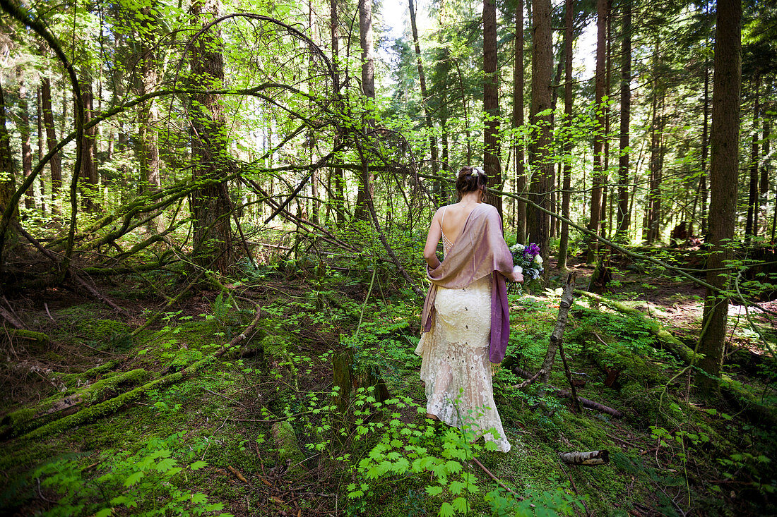 A woman in a dress holds a bouquet of flowers in a forest setting.