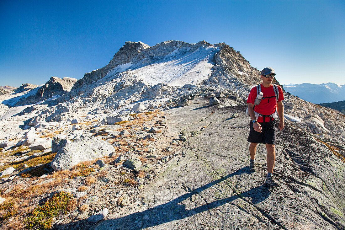 A backpacker hikes from Cassiope Peak towards Saxifrage Peak during a traverse trip near Pemberton, British Columbia, Canada.