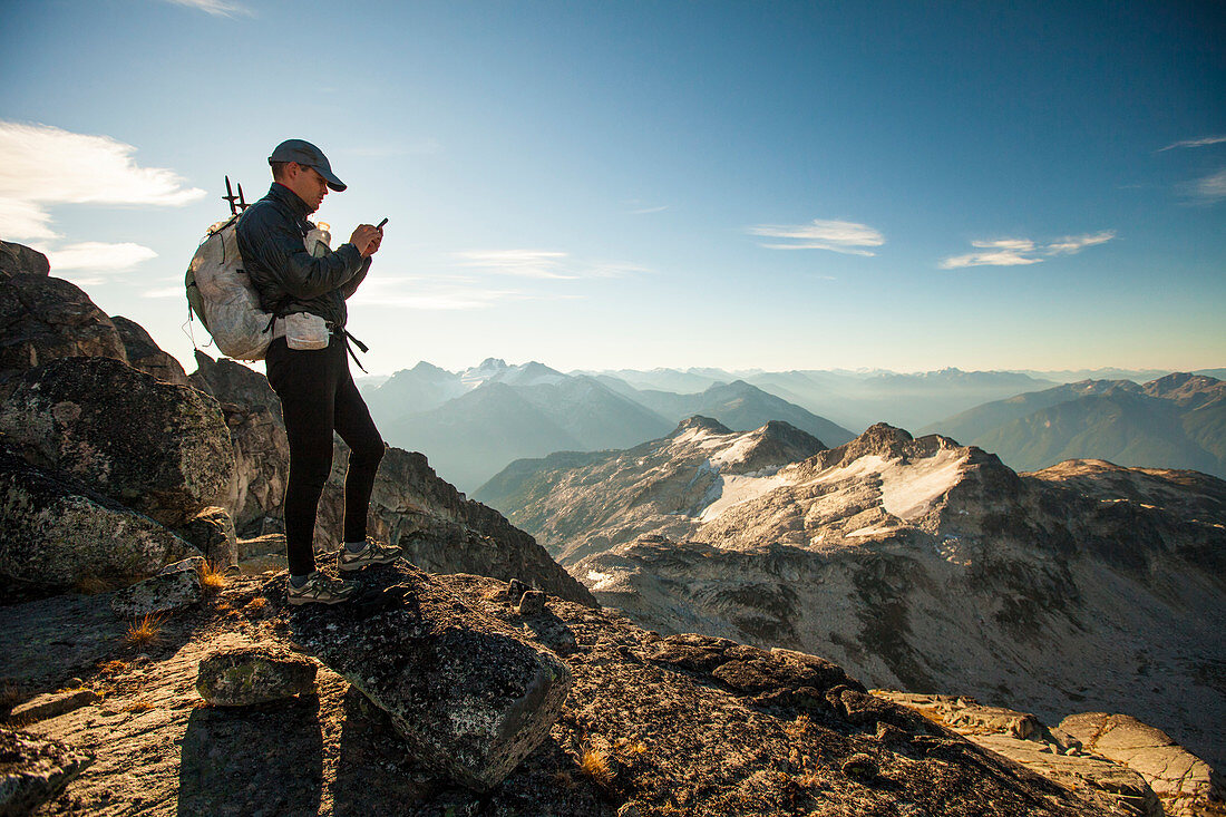 An ultralight backpacker sends a safety message from his smartphone while hiking high in the mountains near Whistler, BC, Canada.