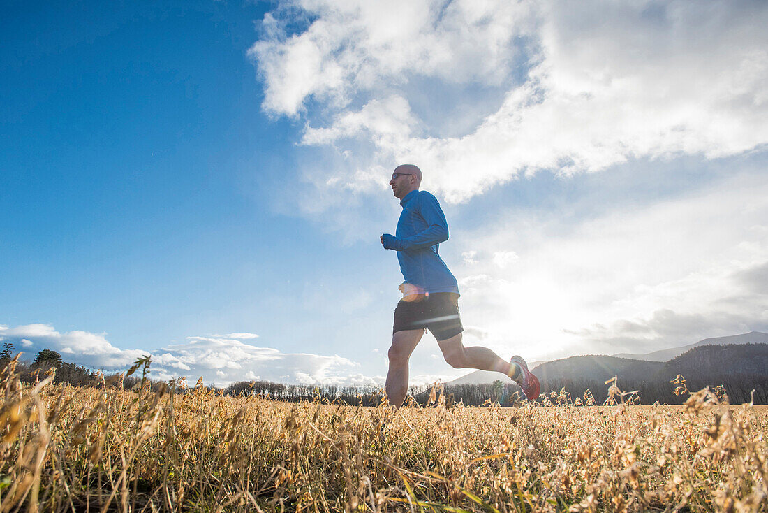 Cunchine peaking through teh clouds as runner goes through a field.