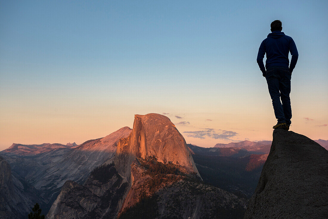 Man standing on a rock looking at Half Dome in sunset light. Yosemite, CA, USA.