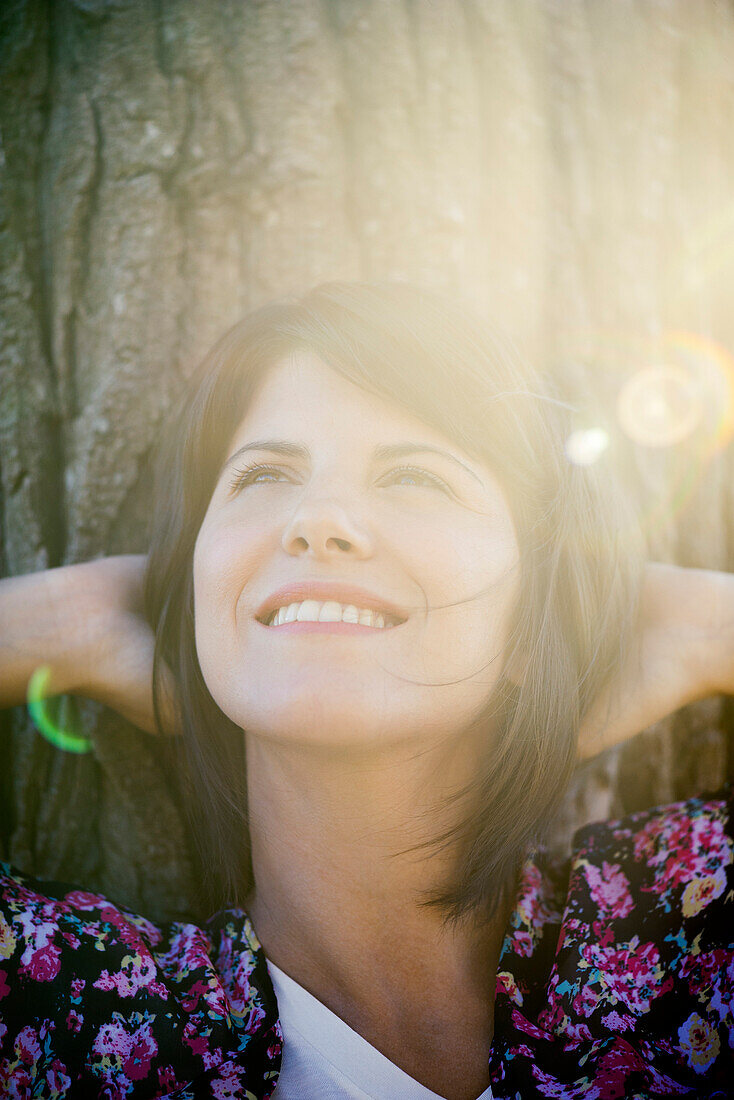 Woman leaning against tree trunk, smiling cheerfully