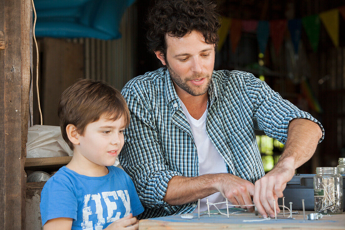 Father watching as young son creates art project with nails and string