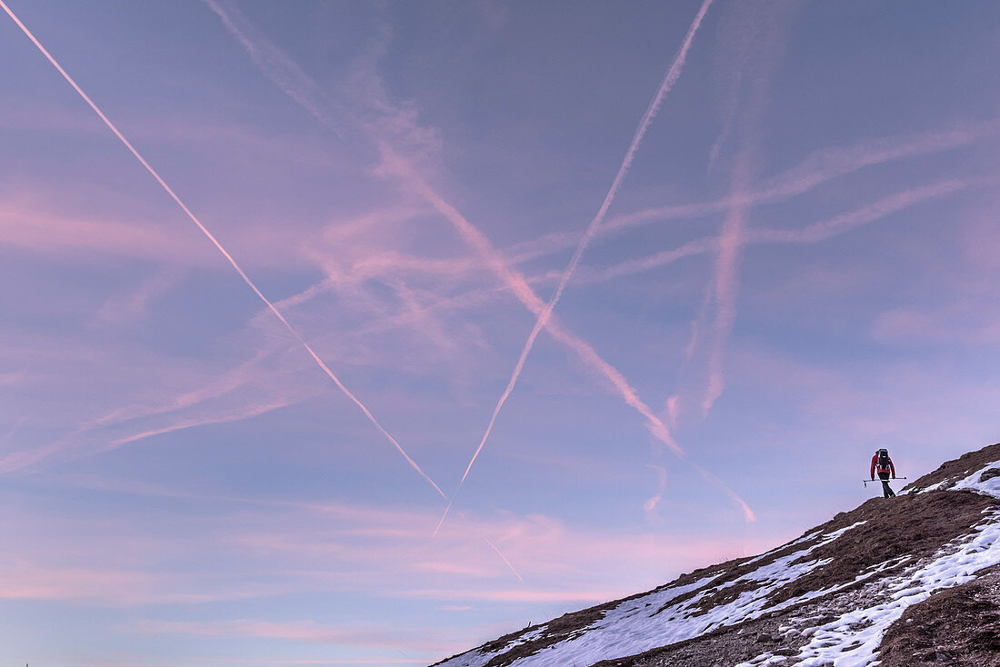 Hiker on winter hiking trailGermany in front of red colored sky with crossing contrails, Oberstdorf, Allgaeu