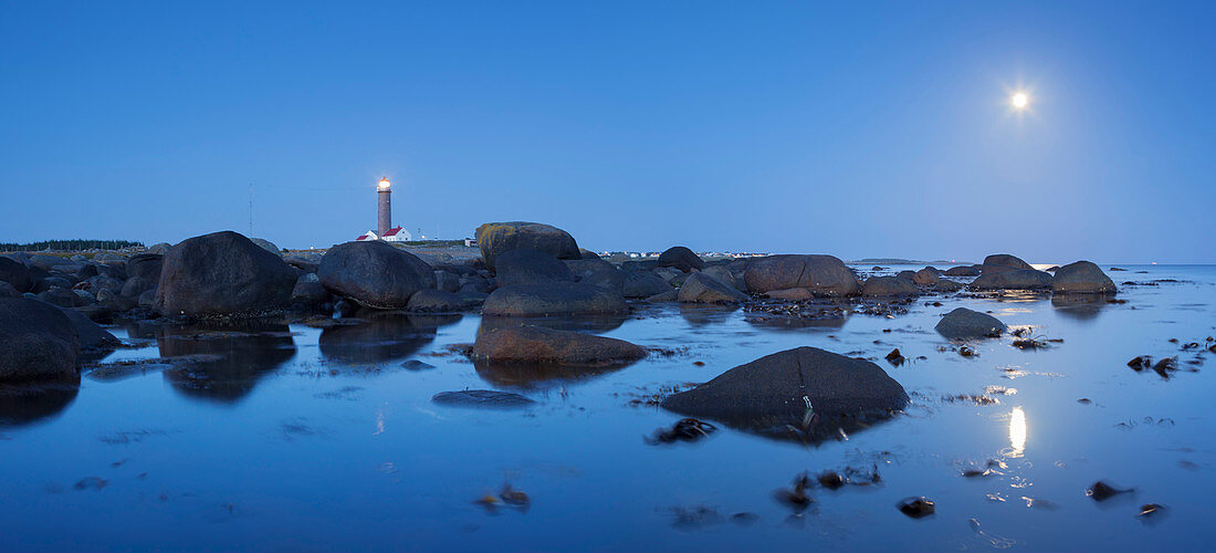 Sanfte Küste der Nordsee mit dem Leuchtturm Lista fyr zwischen Findlingen im Blau der Dämmerung mit Mond, Farsund, Vest-Agder, Norwegen, Skandinavien