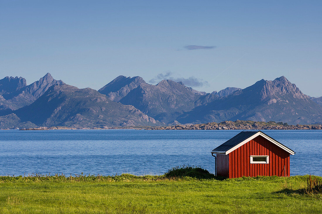 Red boathouse at the ocean with mountains in the background in summer, Skånland, Troms, Norway, Scandinavia