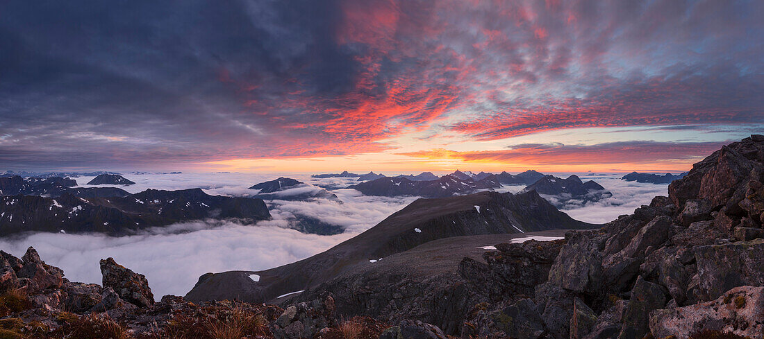 Blick vom Gipfel des Skårasalen ( 1542 m) mit eindrucksvollem Sonnenuntergang über den Wolken und den Bergen der Sunnmøre Alpen mit Felsen im Vordergrund, Møre og Romsdal, Norwegen, Skandinavien