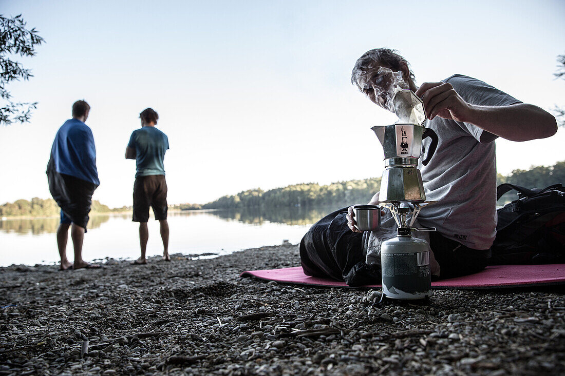 Junger Camper macht Kaffee mit einem Campingkocher, Freilassing, Bayern, Deutschland