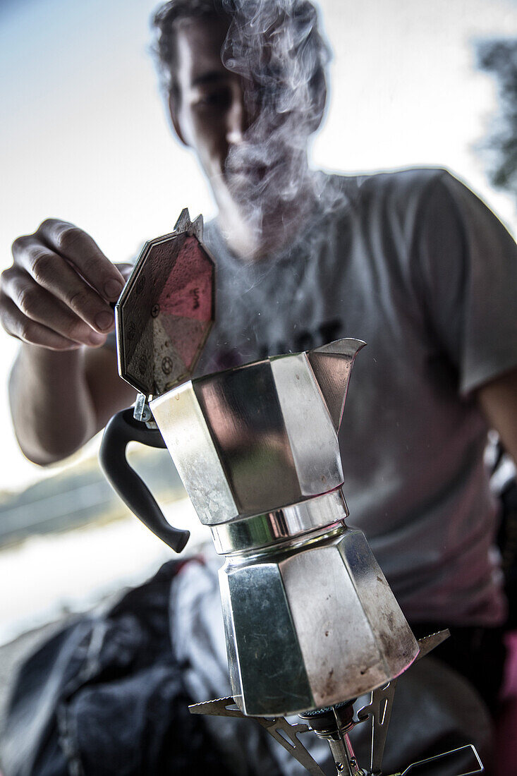 Junger Mann macht Kaffee mit einem Campingkocher, Freilassing, Bayern, Deutschland