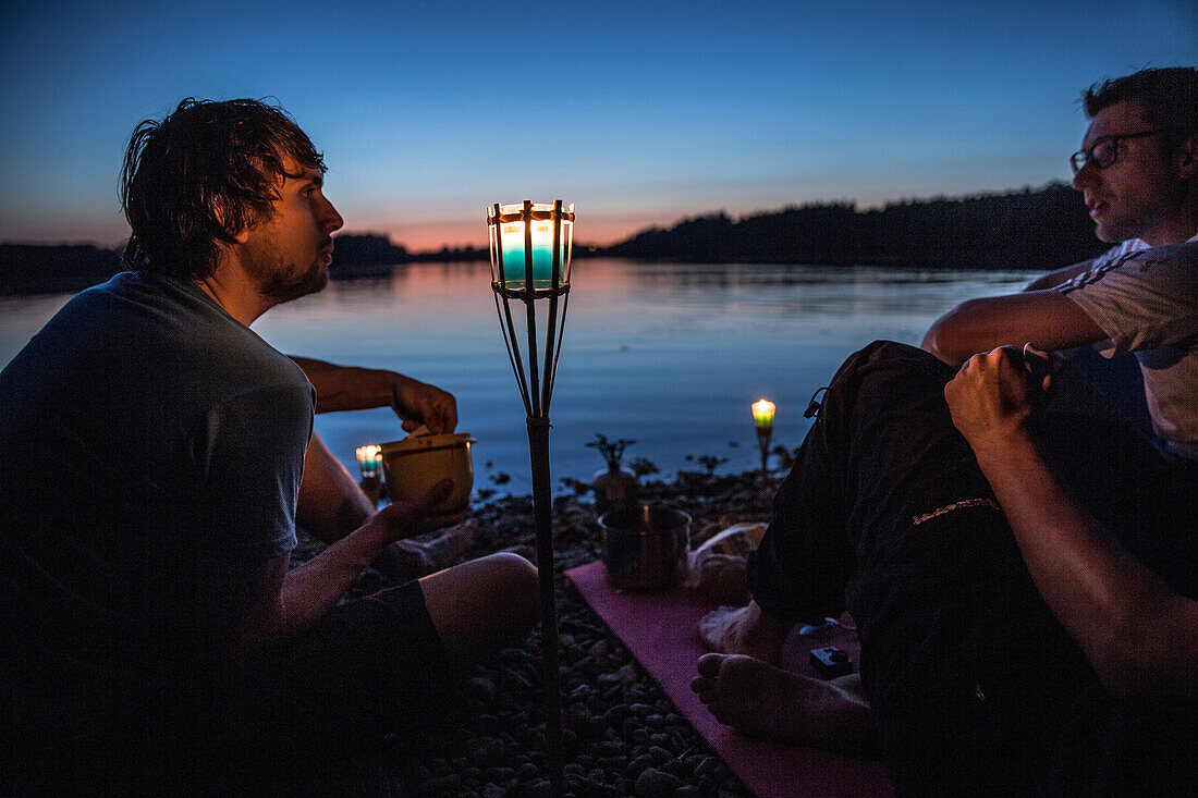 Drei junge Männer sitzen an einem See in der Nacht, Freilassing, Bayern, Deutschland