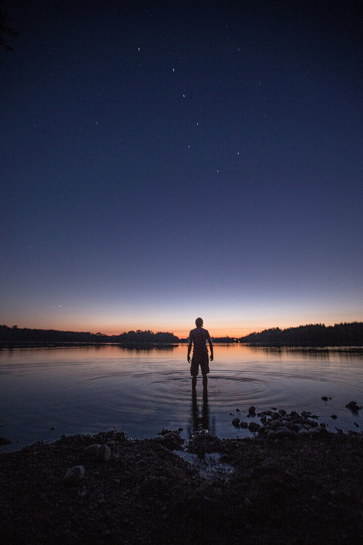 Junger Mann steht in einem See bei Nacht, Freilassing, Bayern, Deutschland