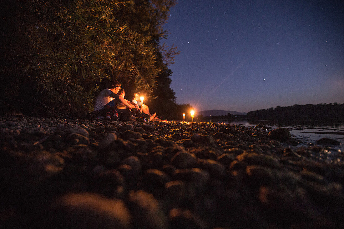 Drei junge Männer sitzen an einem See bei Nacht, Freilassing, Bayern, Deutschland