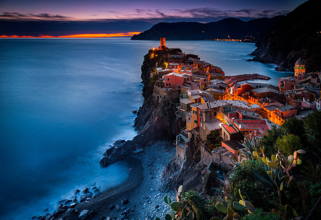 Vernazza, Liguria, Italy. View of the village during sunset, with trees on the foreground and the sea on the background.
