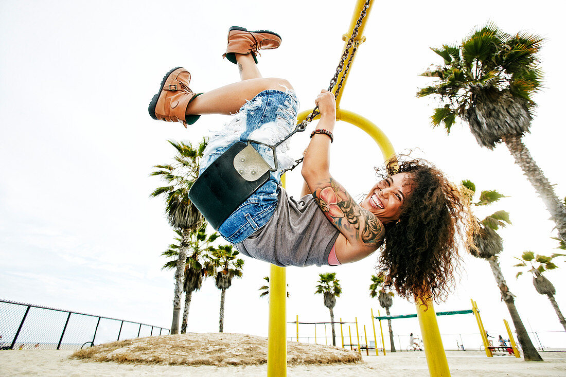 Mixed race woman playing on swing at beach