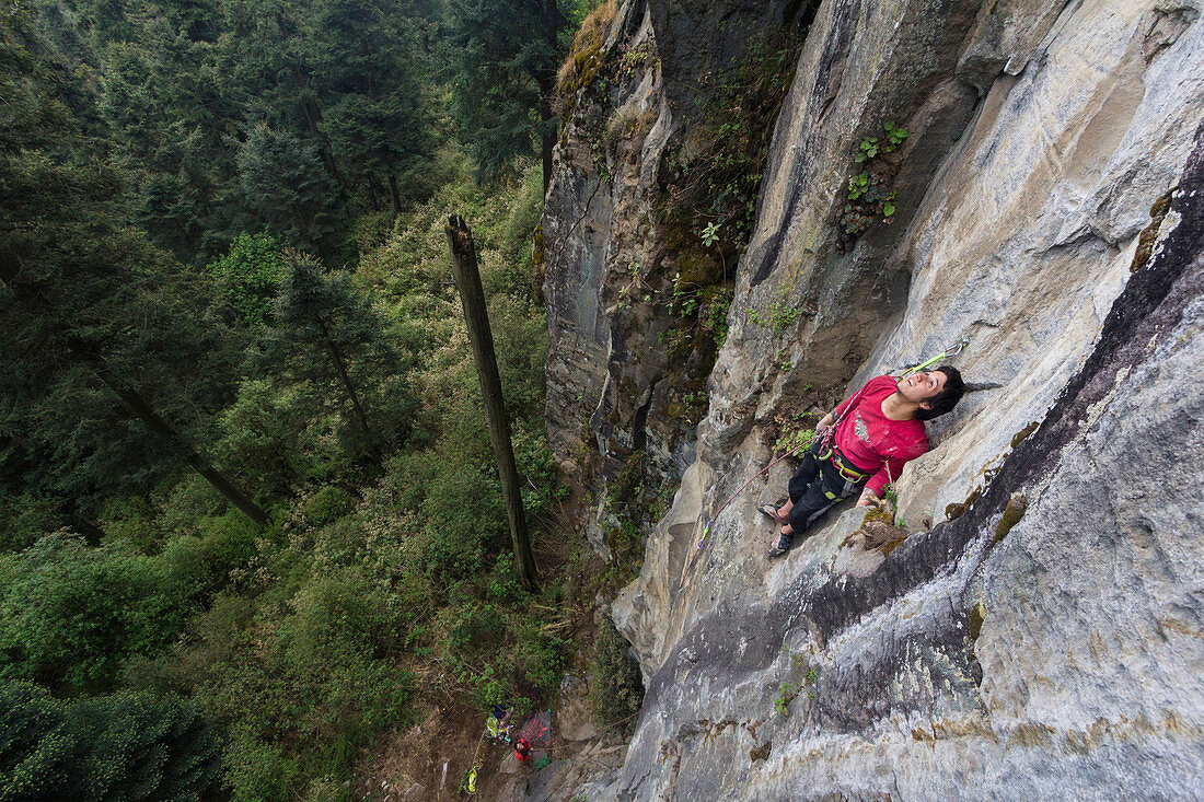 A young male climber dressed in red takes advantage of a ledge to examine the upcoming section of his climb in Los Dinamos, Mexico City, Mexico.