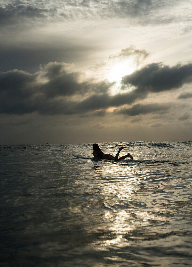 A female surfer paddles out as the sun sets at Newport Beach, Calif.
