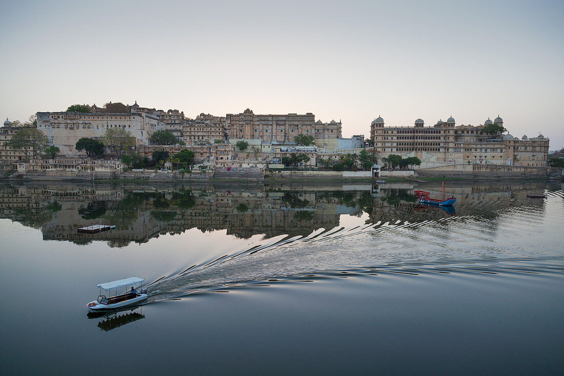 A water taxi passing the City Palace reflected in the still dawn waters of Lake Pichola, Udaipur, Rajasthan, India, Asia