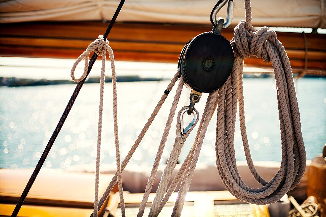 Foreground of pulley and ropes and the boom and mainsail in the background of a vintage yacht moored at Port Mahón, Menorca, Balearic Islands, Spain, Europe