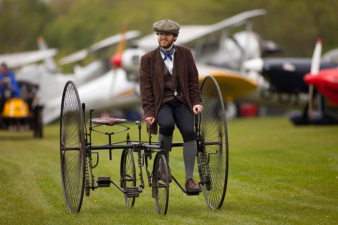 a man wearing Edwardian costume pushes a vintage museum piece Quadracycle, part of the Shuttleworth Collection, at an air display at Old Warden airfield,Bedfordshire,Britain.