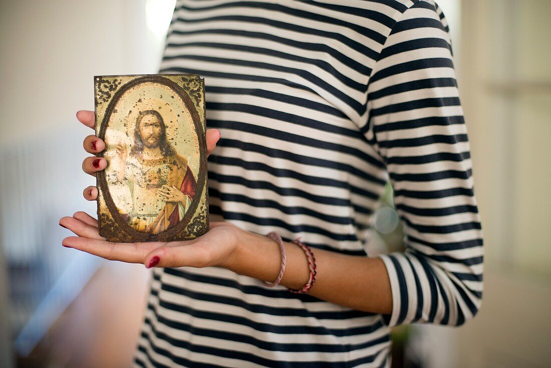 Closeup of young woman with striped shirt showing on their hands a picture of Jesus, Sacred Heart of Jesus