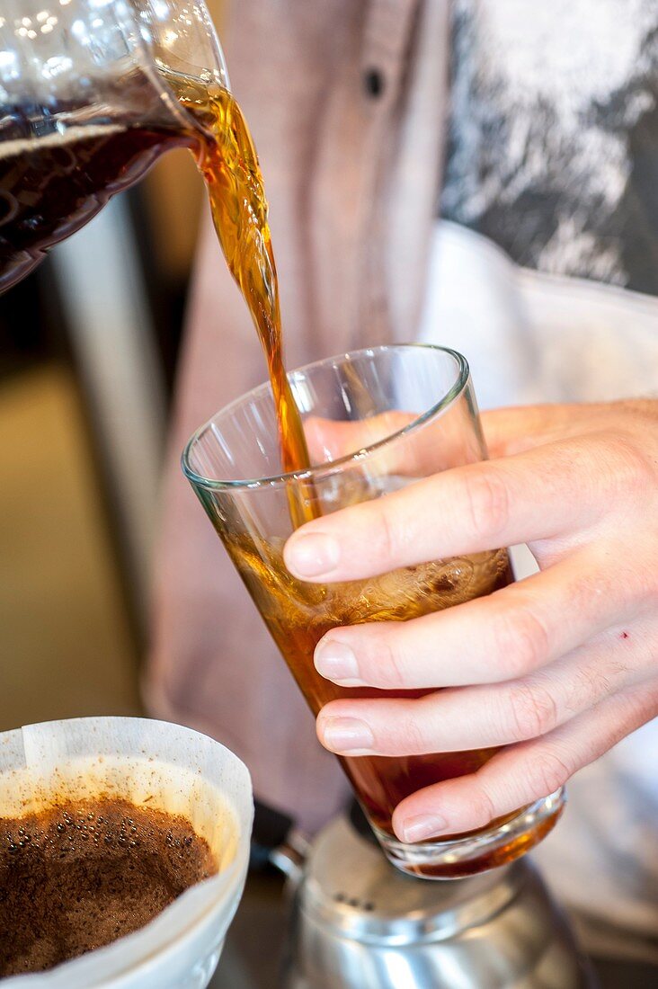 Close up of a person pouring iced coffee into a glass.