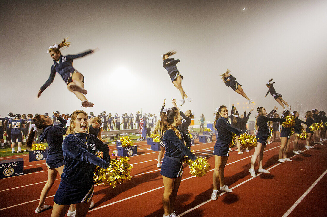 'Cheerleaders entertain the spectators at a high school night football game in San Juan Capistrano, CA, hold initials of the school name. Note ''flyers'' on shoulders of other cheerleaders.'