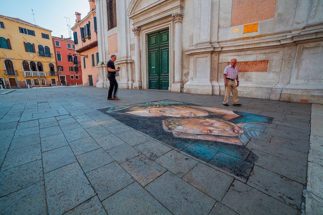 Artwork of a madonnaro in front of the church of Santa Fosca in Venice with two men looking it.