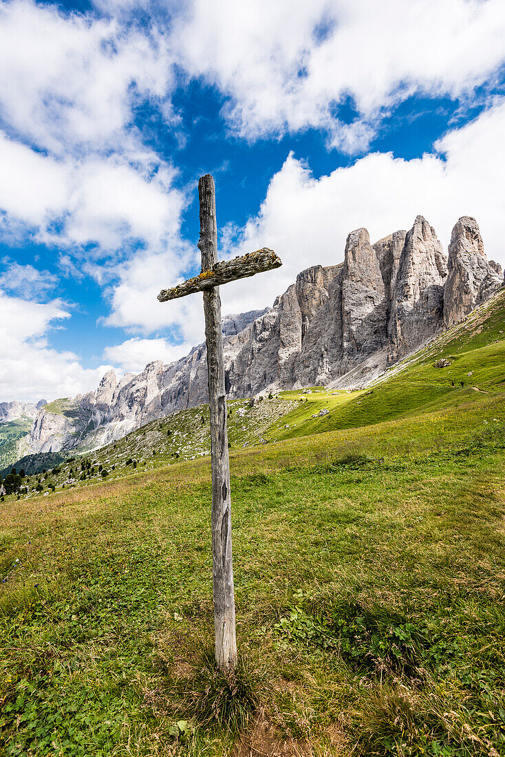 A big wooden cross beside a footpath in front of the mountain scenery at the Sellajoch, Canazei, the Dolomites, South Tirol, Alto Adige, Italy