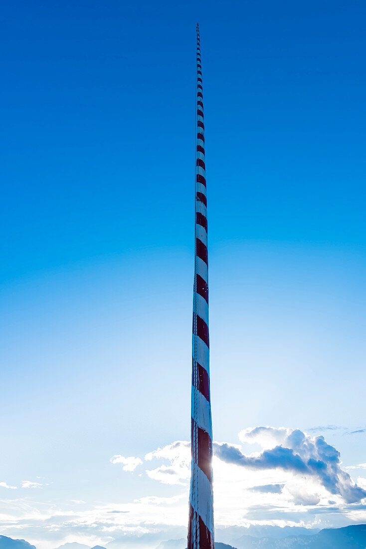 Ein typischer rot weiß geringelter Fahnenmast vor blauem Himmel und einer Bergkulisse, Radein, Südtirol, Alto Adige, Italien