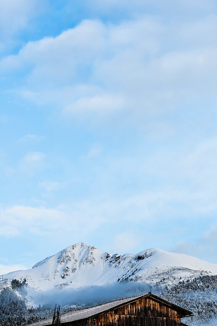 View at the mountain slope with Schwarzhorn, black horn and a wooden hut in the foreground with blue sky after fresh snow, Radein, South Tirol, Alto Adige, Italy