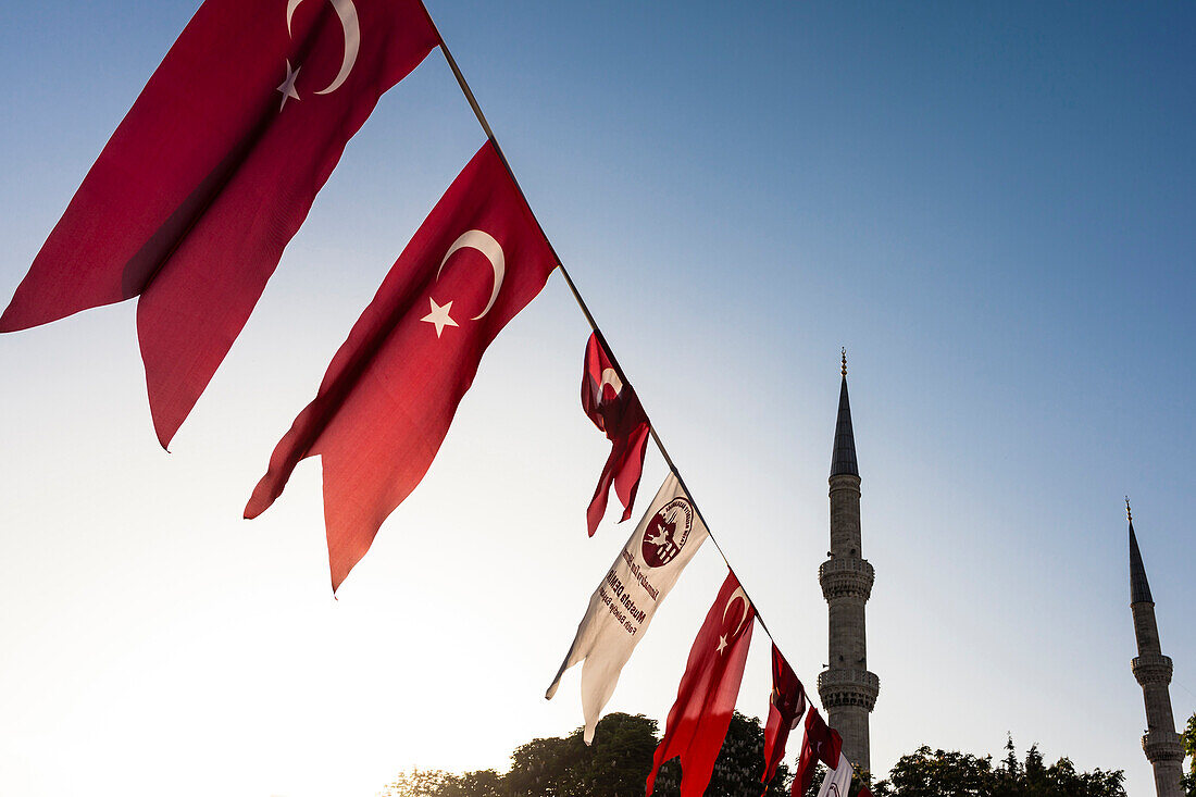 Die Minarette der Blauen Moschee, Sultan-Ahmed-Moschee, im Morgenlicht zwischen den Nationalflaggen die über dem Hippodrom hängen, Istanbul, Türkei