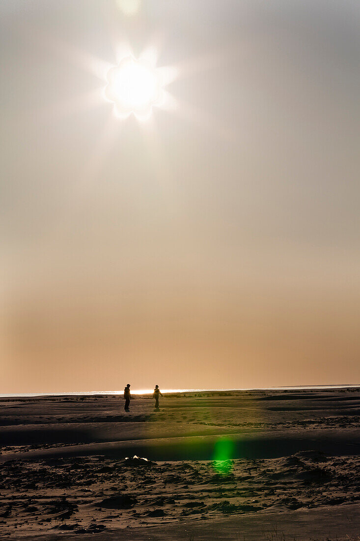 Ein Pärchen am weitläufigen Sandstrand im Gegenlicht der Sonne, Amrum, Schleswig Holstein, Deutschland