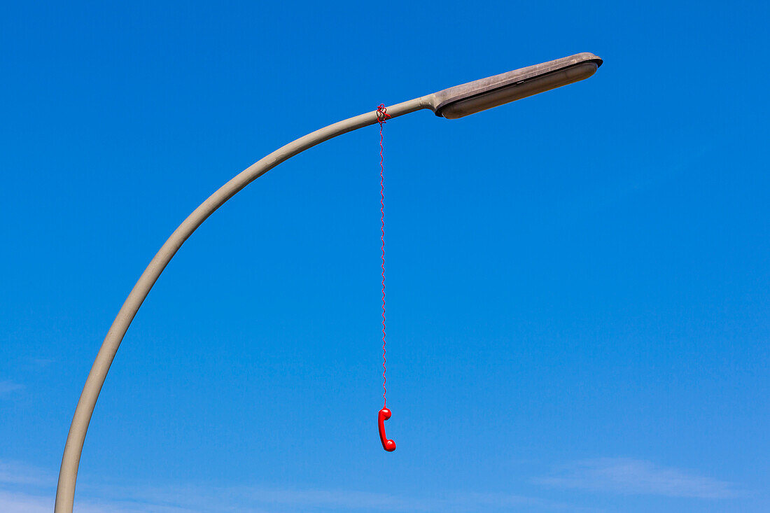 Ein roter analoger Telefonhörer hängt an einer Straßenlaterne, Hamburg, Deutschland