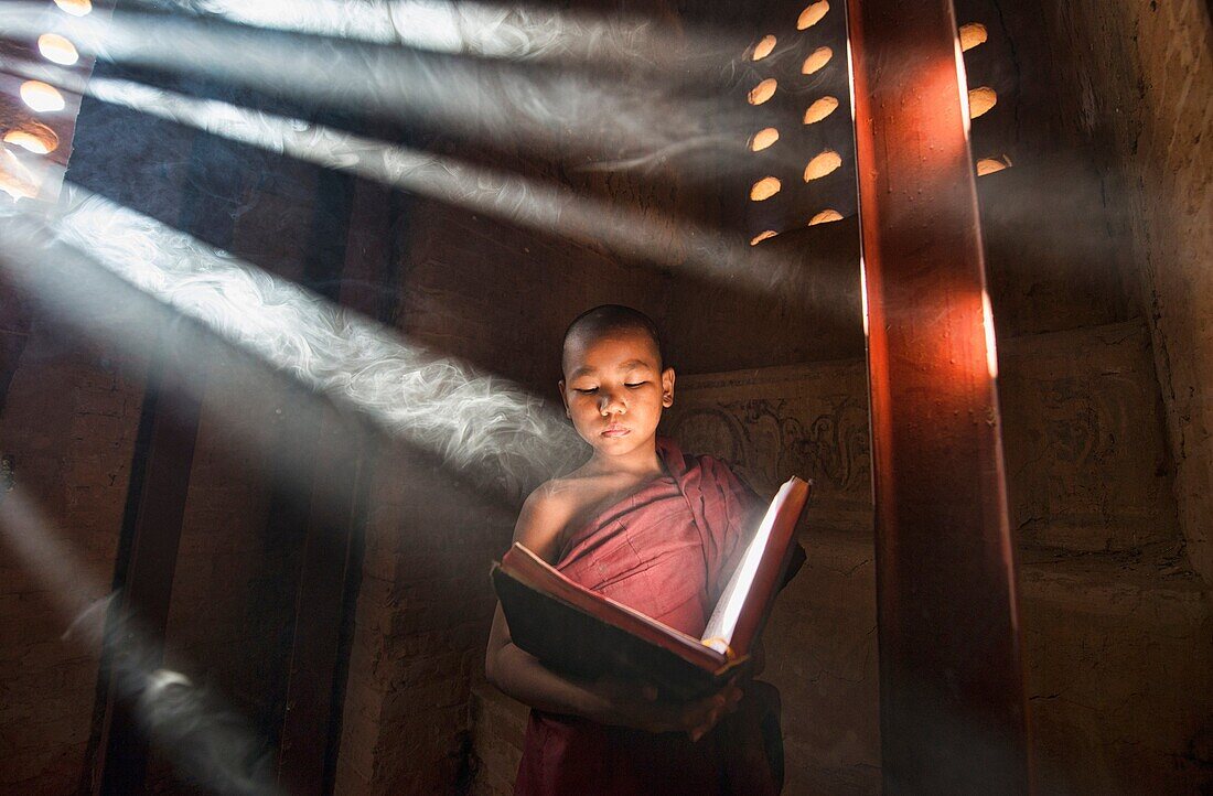 A young monk reading with rays of sunlight in the temples of Bagan, Myanmar.