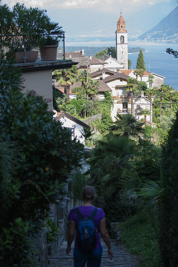 Junge Wanderin geht Treppen zu einer alten Stadt am See hinunter, Ronco, Tessin, Schweiz