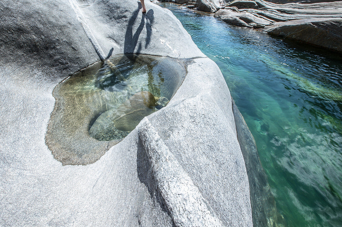 Young female hiker walking on rocks between a river, Valle Verzasca, Ticino, Switzerland