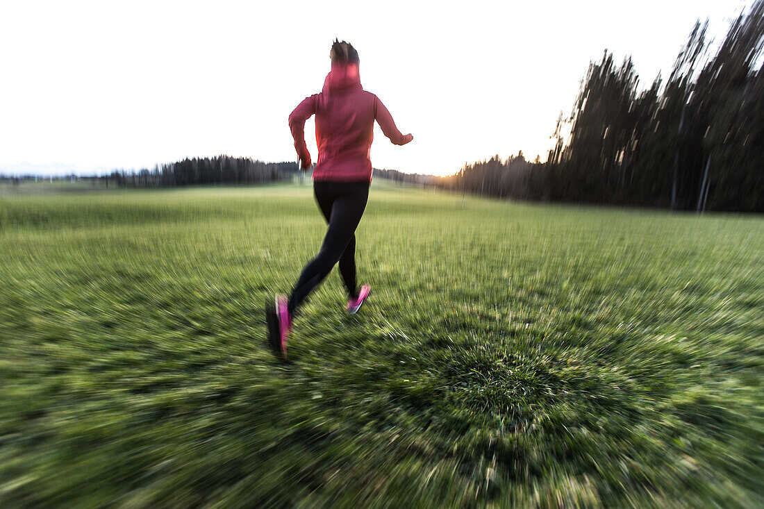 Junge Frau läuft über ein Feld, Allgäu, Bayern, Deutschland
