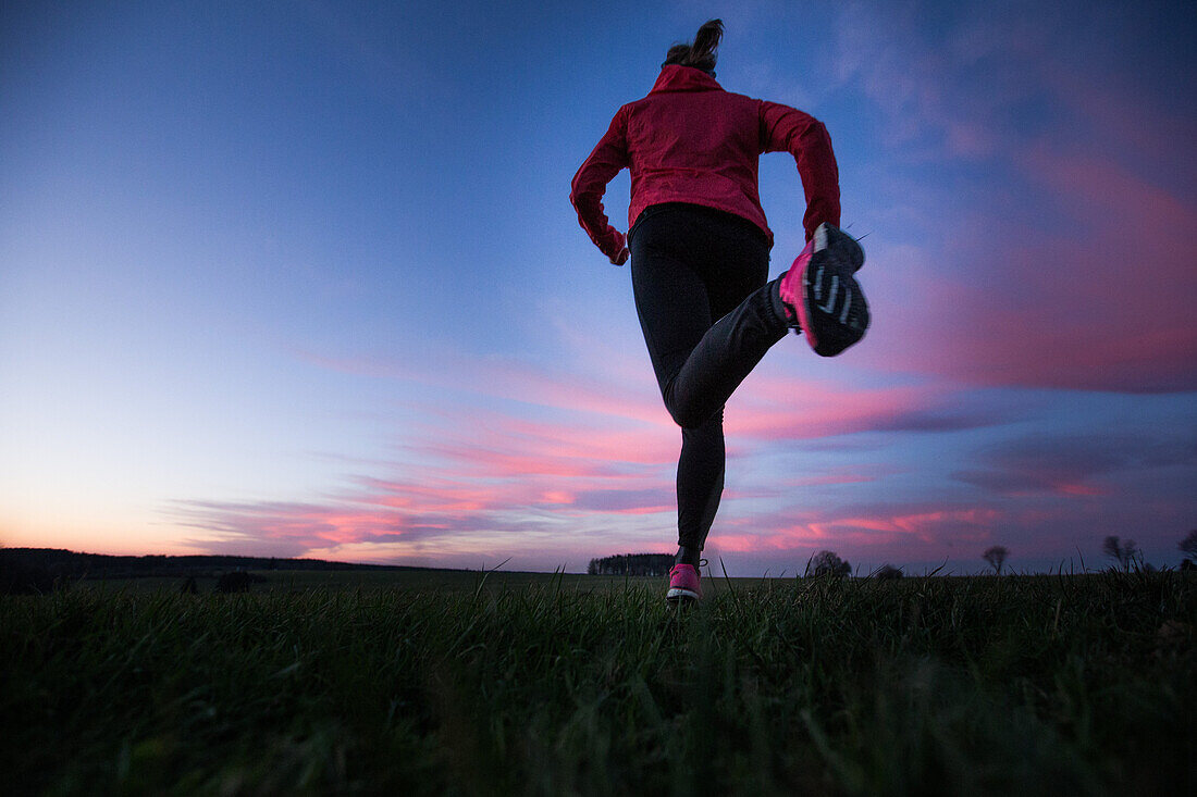 Young woman running over a field at sunset, Allgaeu, Bavaria, Germany
