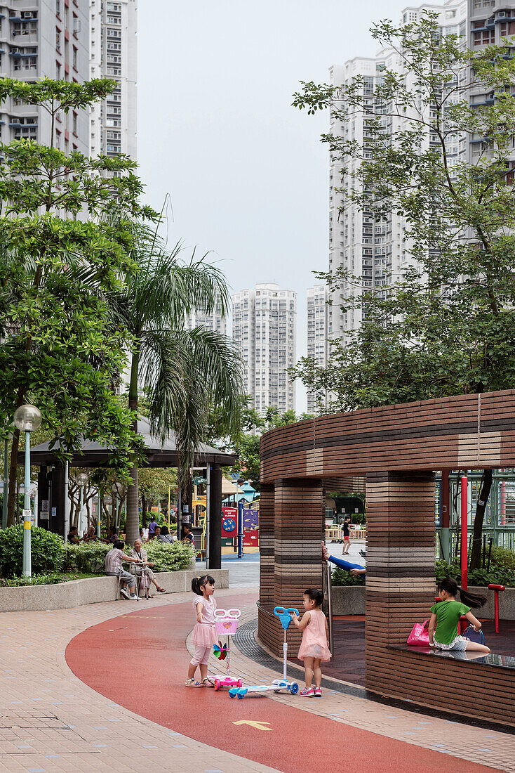 chinese girls dressed in pink play with scooters in one of the residential parks at Tin Shu Wai, Hongkong, China, Asia