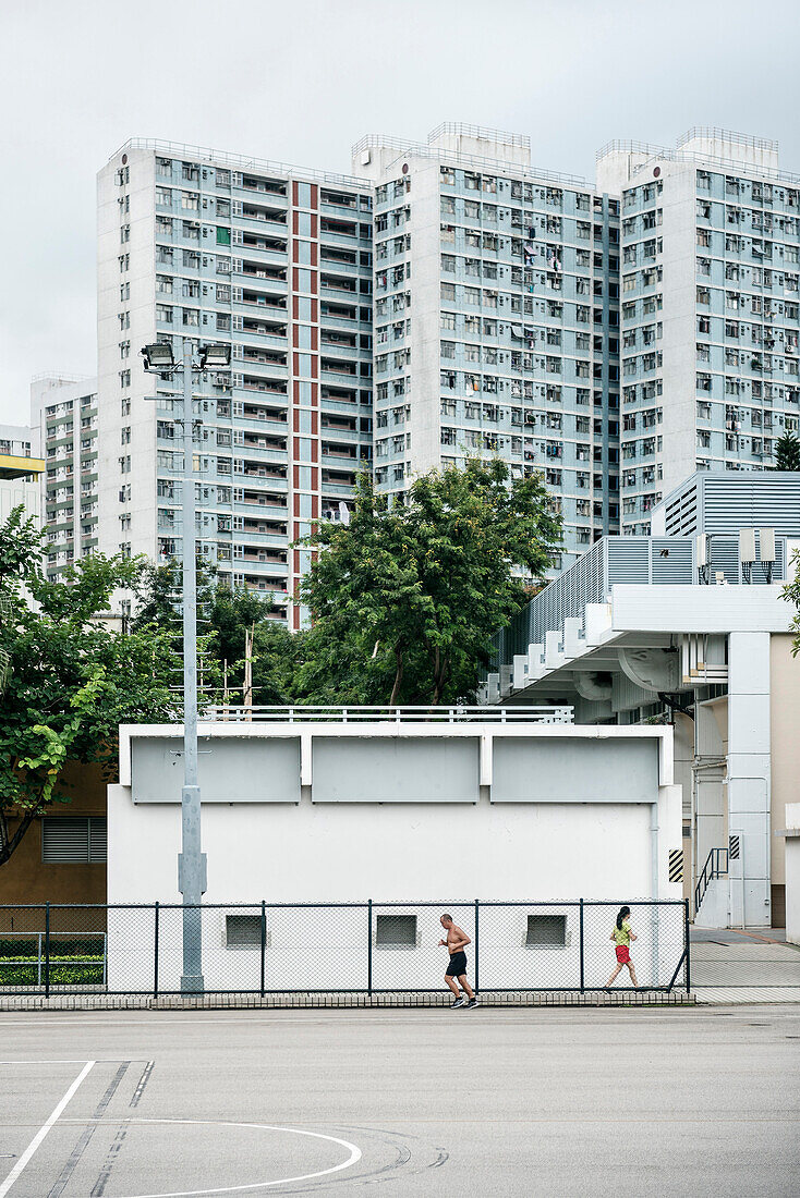 Mann mit nacktem Oberkörper und Frau joggen in einem Park vor Hochhäusern, Kowloon, Hongkong, China, Asien