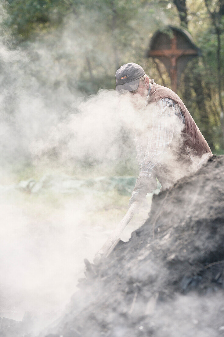 charcoal burner wokrs on smoking kiln, charcoal production, Aalen, Baden-Wuerttemberg, Germany