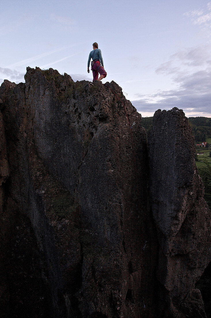 Junge Kletterin steht auf der Spitze eines hohen Felsens, Pottenstein, Franken, Deutschland