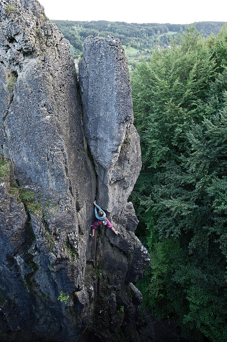 Junge Frau klettert an einer Felswand, Pottenstein, Franken, Deutschland