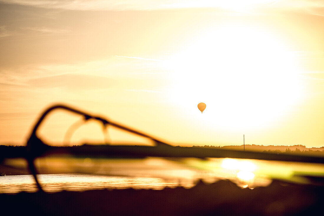 View over a sail at a lake to a hot-air ballon while sunset, Ammersee, Bavaria, Germany